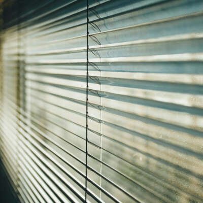 A perspective close-up of horizontal silver Venetian blind slats, showing the thin cord mechanism and soft light filtering through.