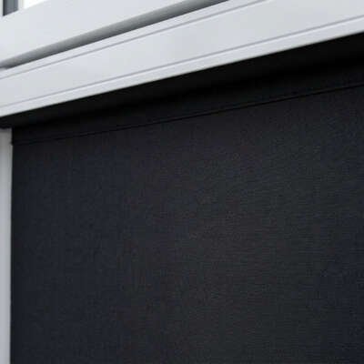 A close-up of a black textured blackout roller blind installed within a white uPVC window frame with a white beaded pull cord.