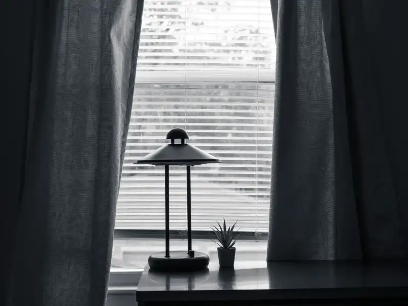 A lamp on a table near a window with a curtain in a dark room.