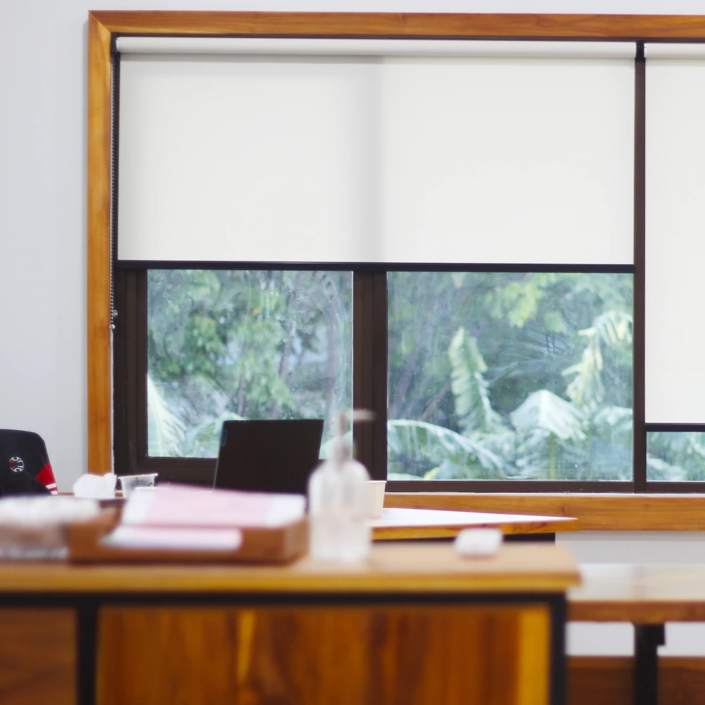 Modern Office Roller Blinds Modern white roller blinds fitted inside a wooden window frame in a bright, professional office space.